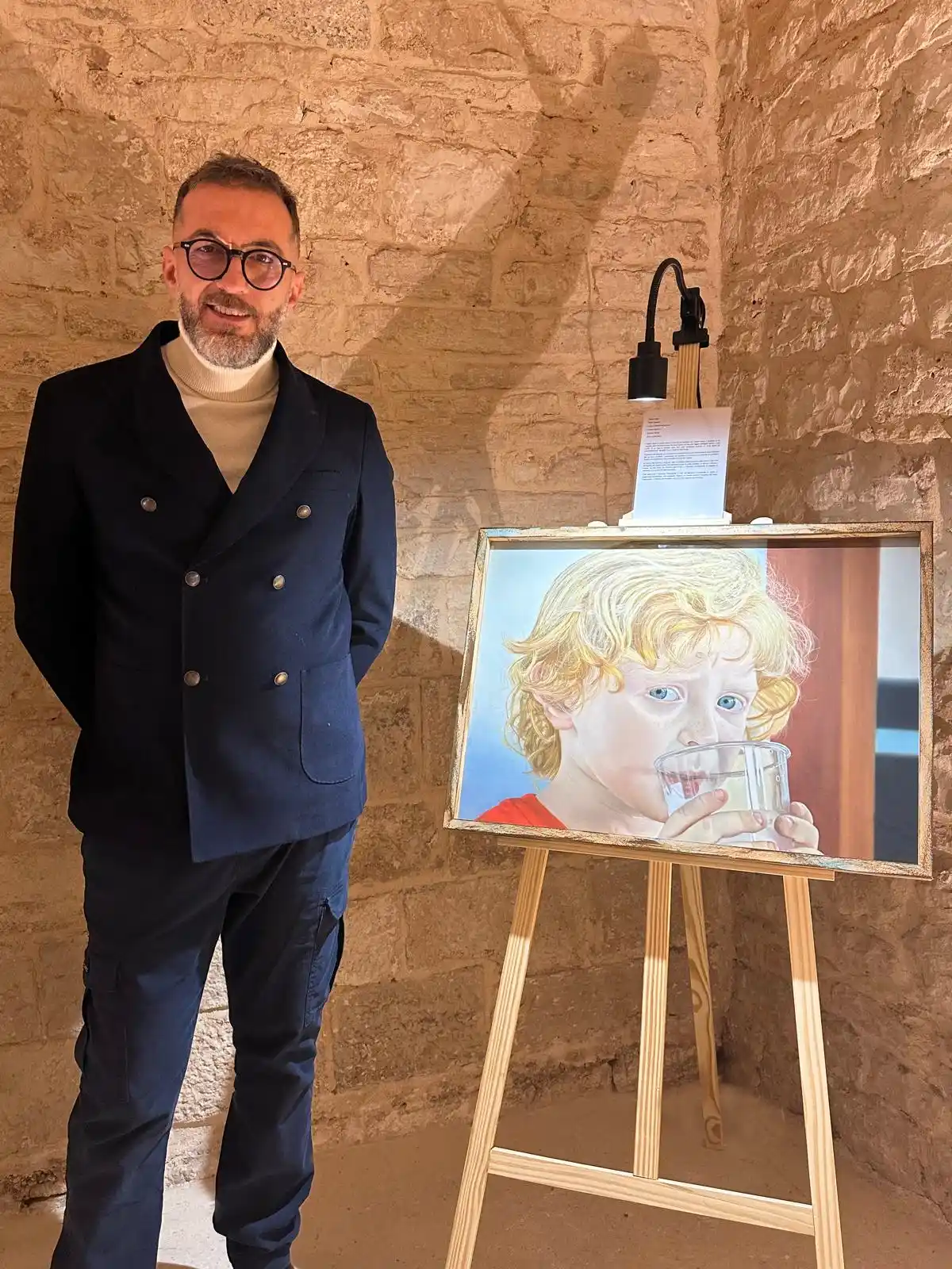 Roberto Mangialardi in una sua Mostra accanto al suo quadro del bambino biondo con occhi azzurri